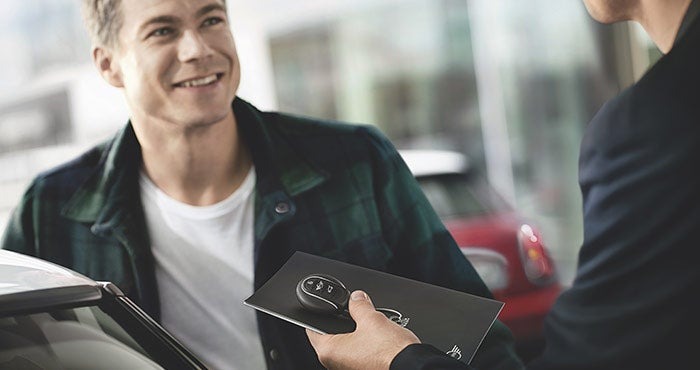 A man in a plaid shirt is smiling while receiving car keys from another person.